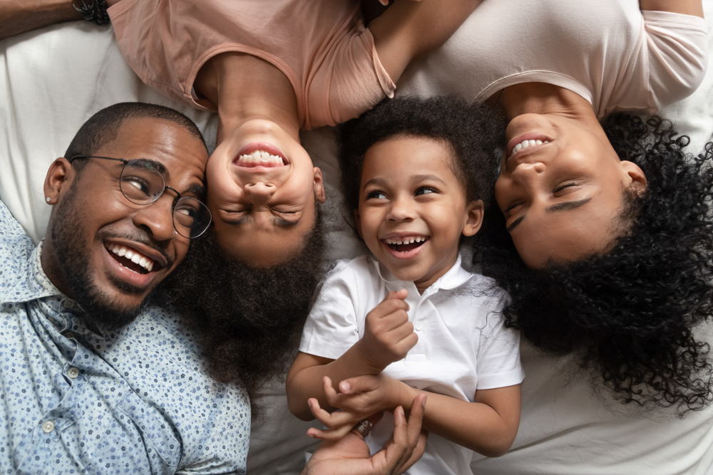 A laughing family of four lies on their backs, showcasing their healthy smiles from cosmetic dentistry in Castle Rock at Castle Rock Family Dental