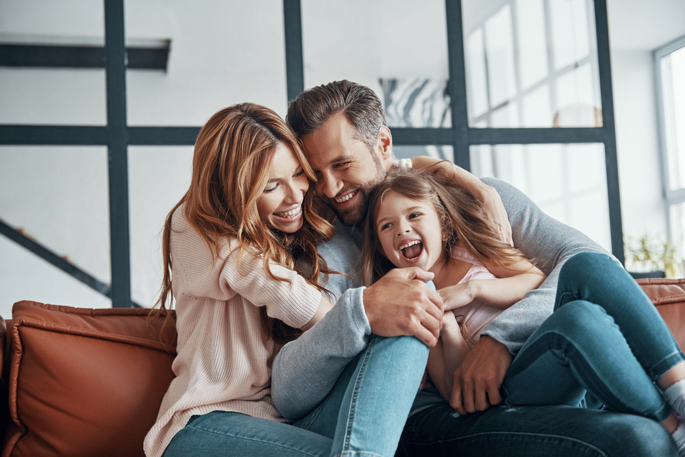 A laughing family of three on a couch, representing general and family dentistry in Castle Rock at Castle Rock Family Dental
