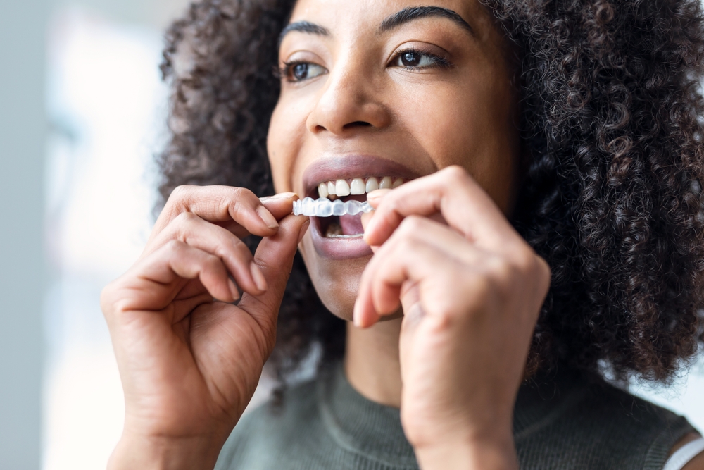A smiling woman holds up clear Invisalign aligners, for treatment in Castle Rock at Castle Rock Family Dental