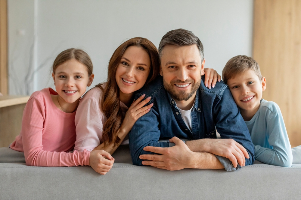 A smiling family of four leans over a couch, showcasing their healthy smiles from preventative dentistry in Castle Rock at Castle Rock Family Dental