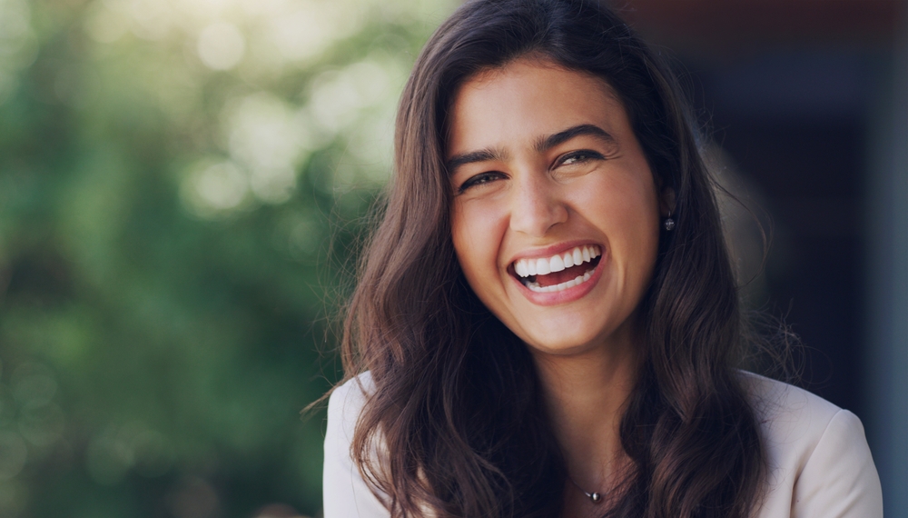 A laughing woman with long dark hair, showing her healthy smile after extraction and preservation at Castle Rock Family Dental
