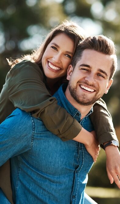 A happy couple smiles as the woman gets a piggyback ride, representing the benefits of a membership plan in Castle Rock at Castle Rock Family Dental